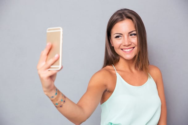 Smiling young girl making selfie photo on smartphone over gray background.jpeg